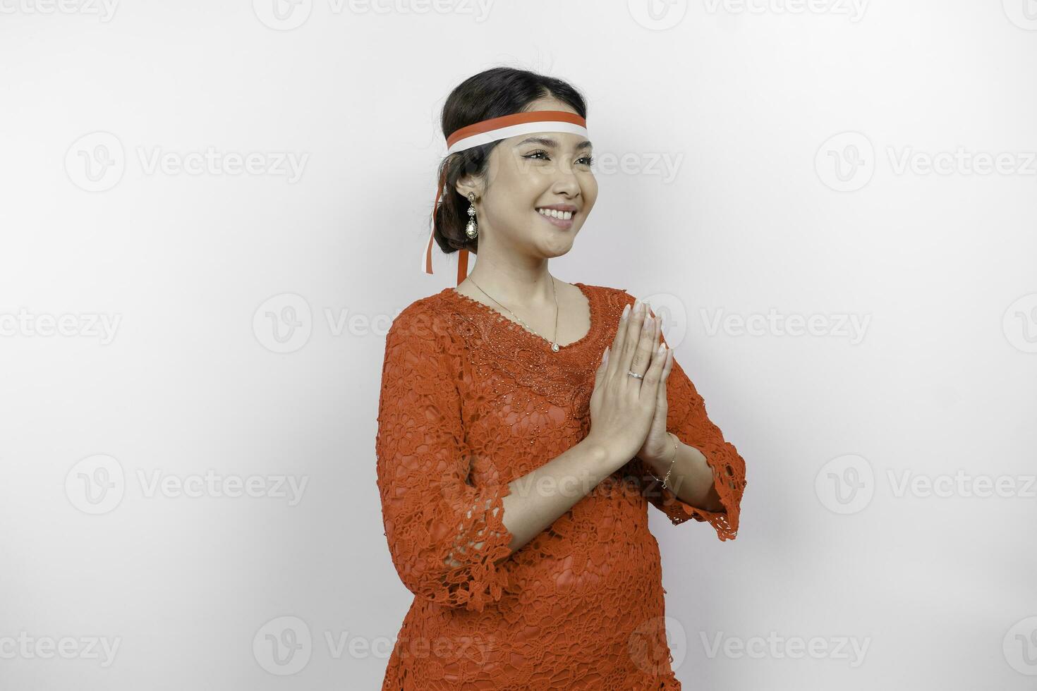 un simpático indonesio mujer es vistiendo rojo kebaya gesticulando tradicional saludo y de indonesia bandera venda a celebrar Indonesia independencia día. aislado por blanco antecedentes. foto