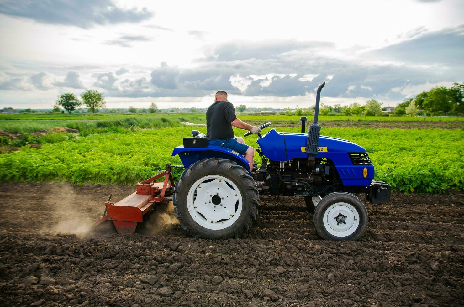 Kherson oblast, Ukraine - May 29, 2021 Farmer on a tractor cleans the field after harvest. Running a small agribusiness. Farm work. Farming. Loosening, land cultivation. Mechanization in agriculture. photo