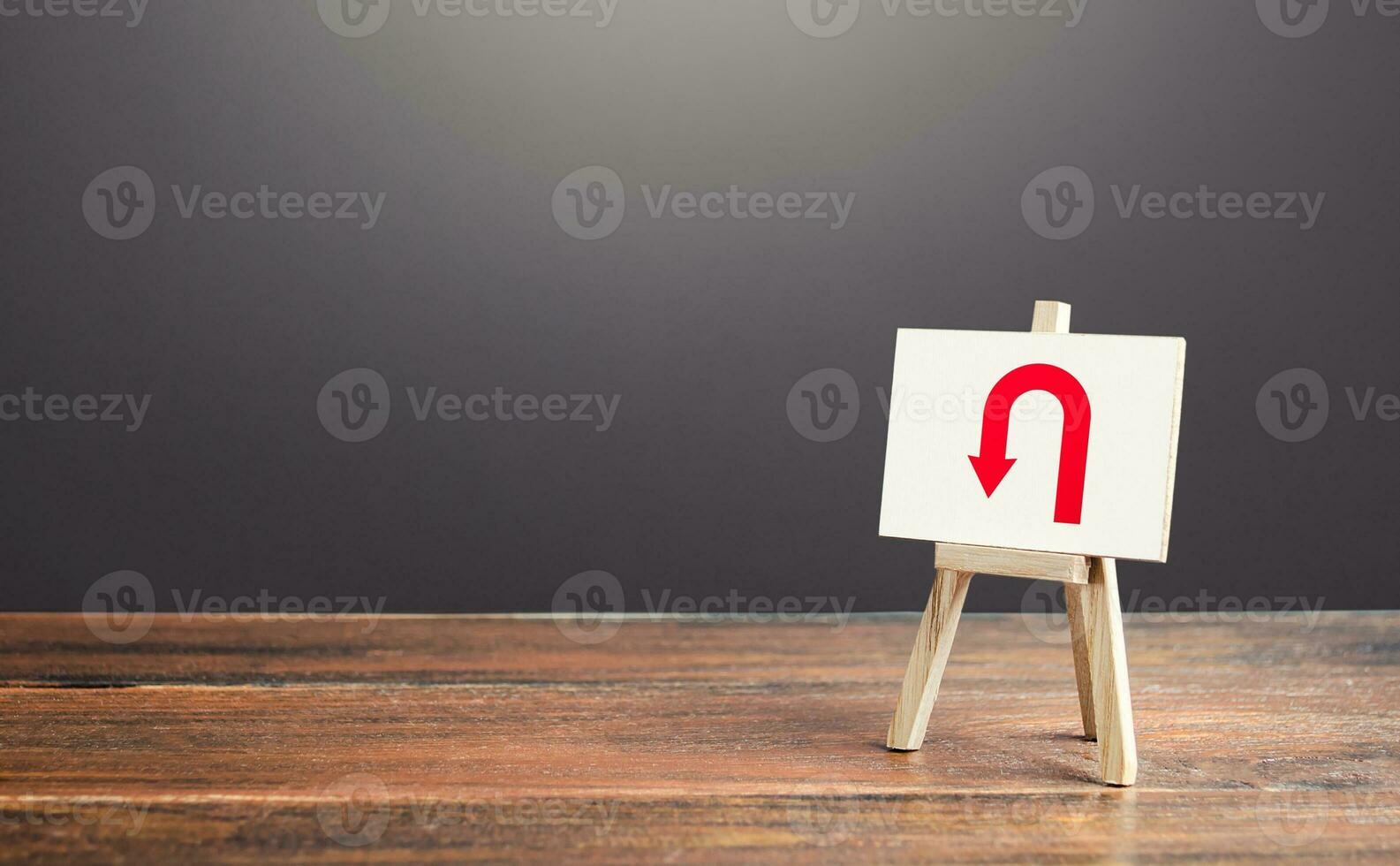 Easel with arrow turning back. Change plans, circumstances. Tactical retreat. Avoiding problems, reducing risks. Find other way. Return to source. Step back. Reassessment of actions. Break a promise. photo