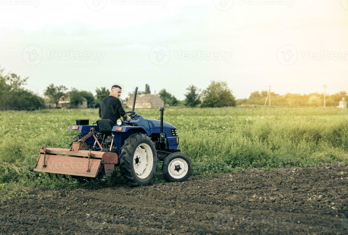 A farmer is driving a tractor across the field. Mill grinding machine for soil. Land cultivation. Recruiting and hiring seasonal worker for work. Farming, agriculture. Land improvement, mitigation. photo