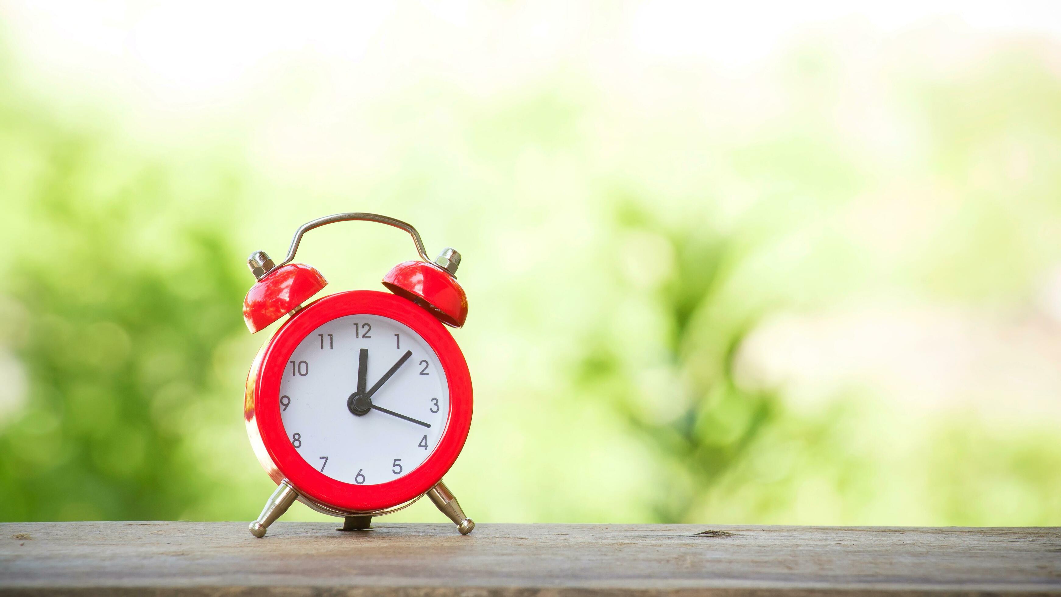 Red alarm clock with green nature background. Time to relax at 12 o