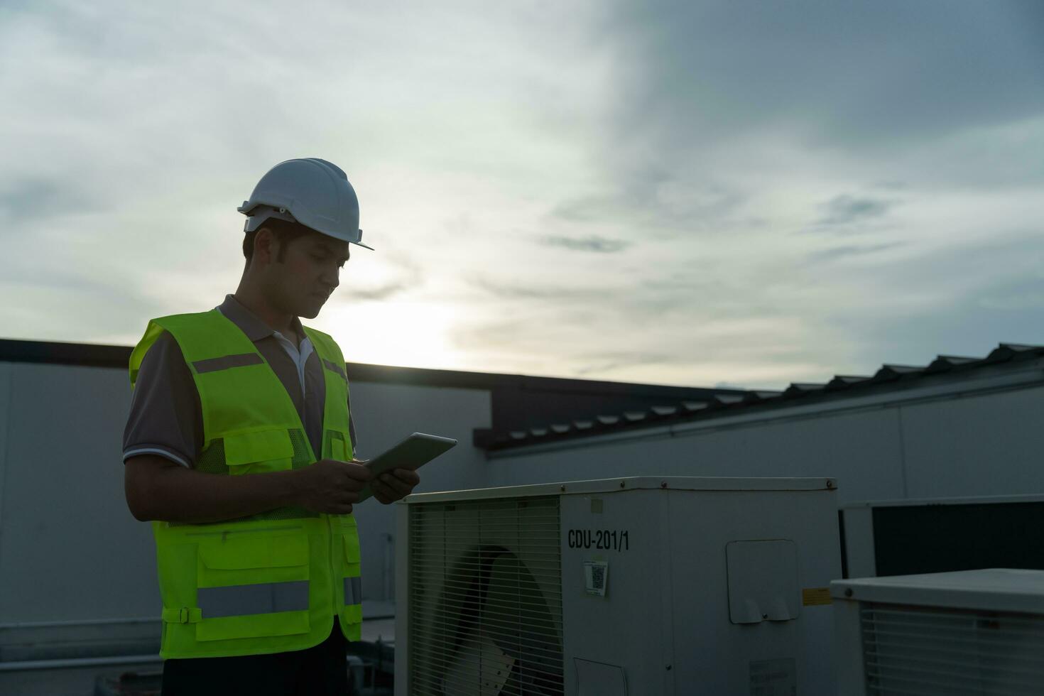 Asian maintenance engineer works on the roof of factory. contractor inspect compressor system and plans installation of air condition systems in construction. technology, online, mobile application. photo