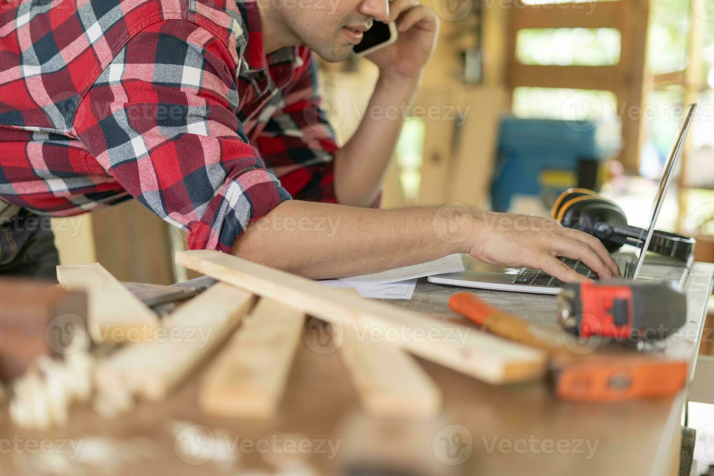 Asian man owner a small furniture business is recheck order online. carpenter male is adjust wood to the desired size. architect, designer, Built-in, professional wood, craftsman, workshop. photo
