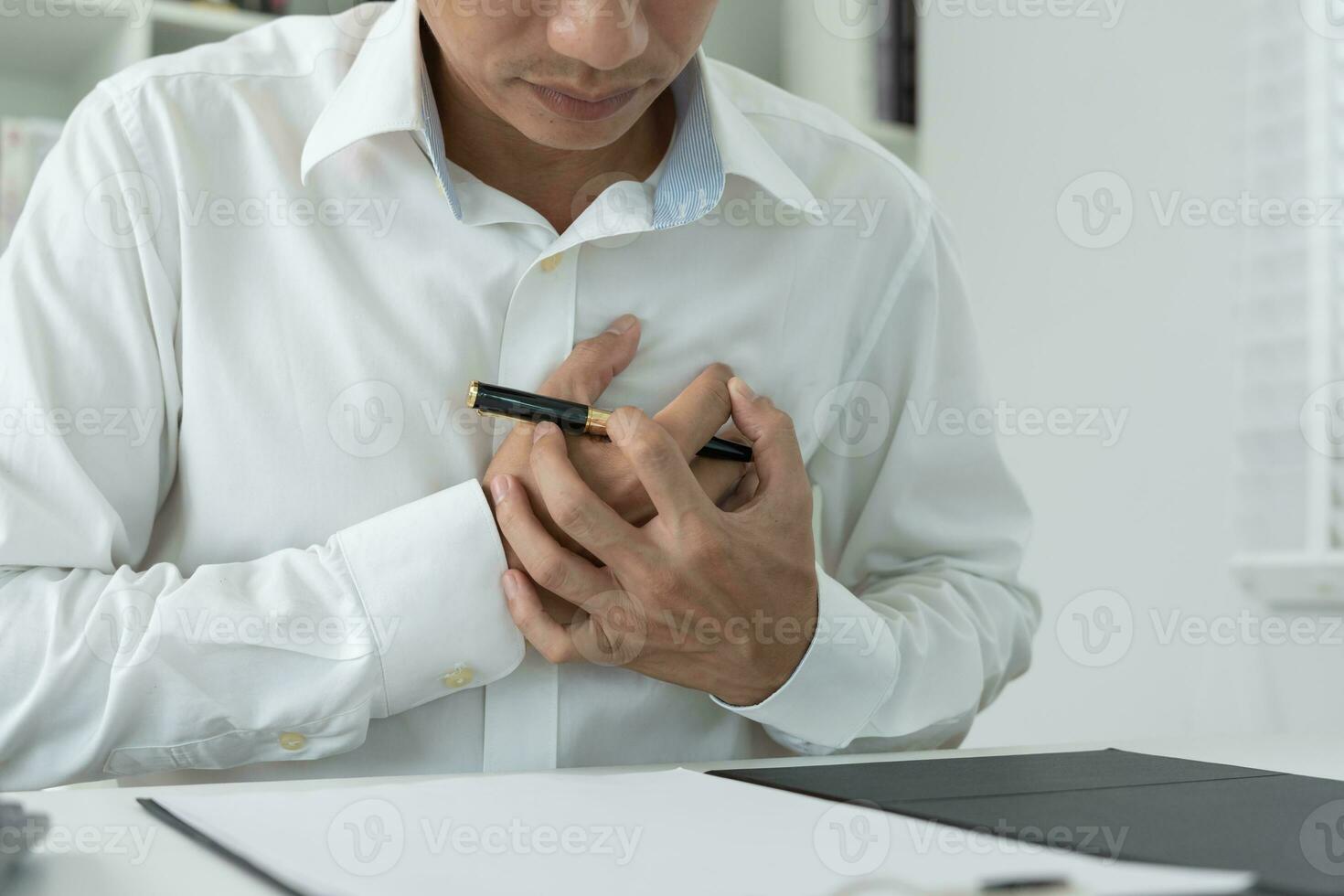 hand hold chest with heart attack symptoms, asian man working hard have chest pain caused by heart disease, leak, dilatation, enlarged coronary heart, press on the chest with a painful expression photo