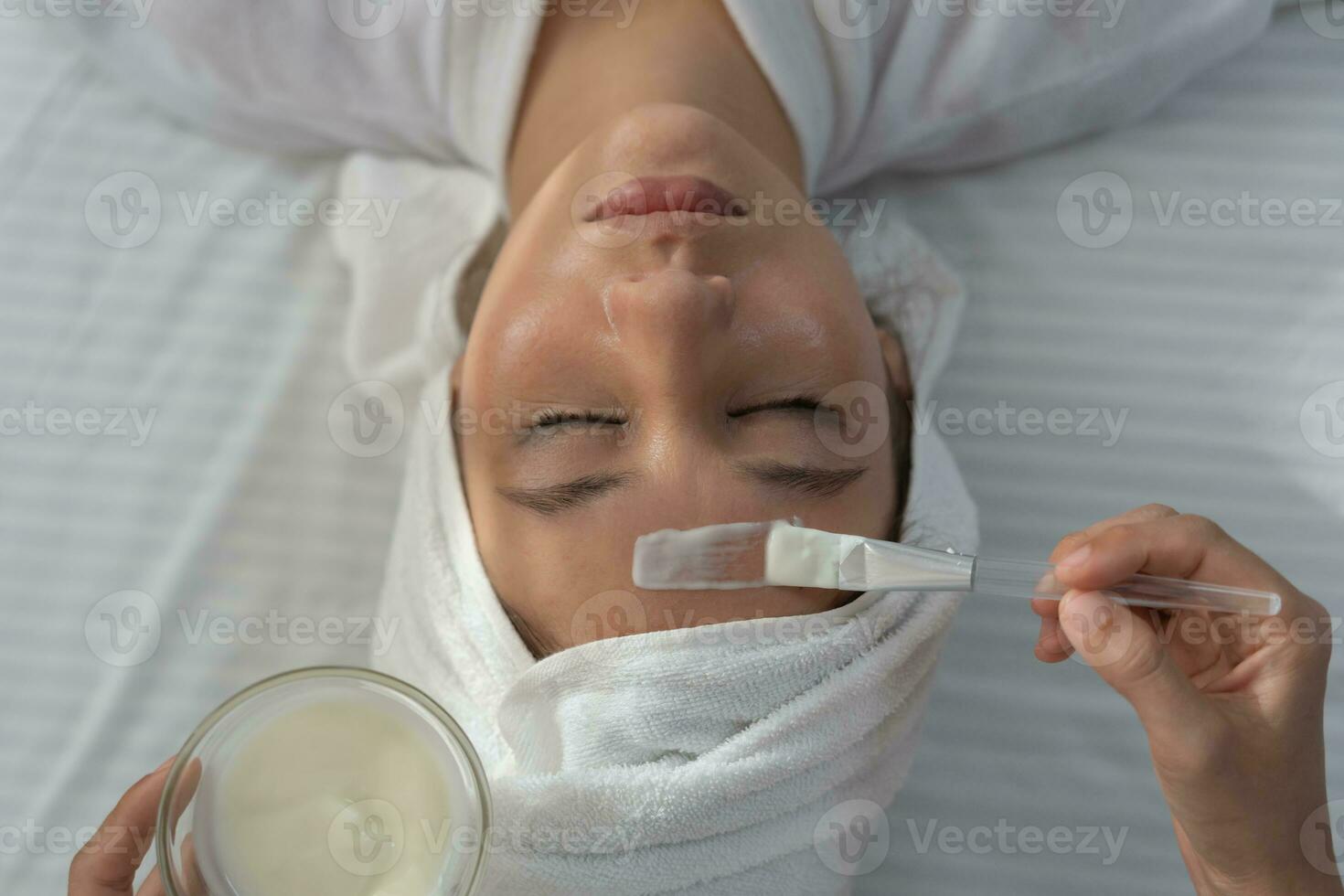 hermosa mujer recibir spa y tratamiento piel de rostro. cara de un sano mujer aplicar crema. anuncio para piel crema, anti arrugas, bebé rostro, blanqueo, hidratante, apretar poros suero foto