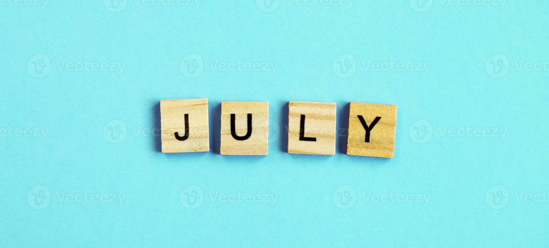 July word made by wooden cubes on a blue turquoise background photo