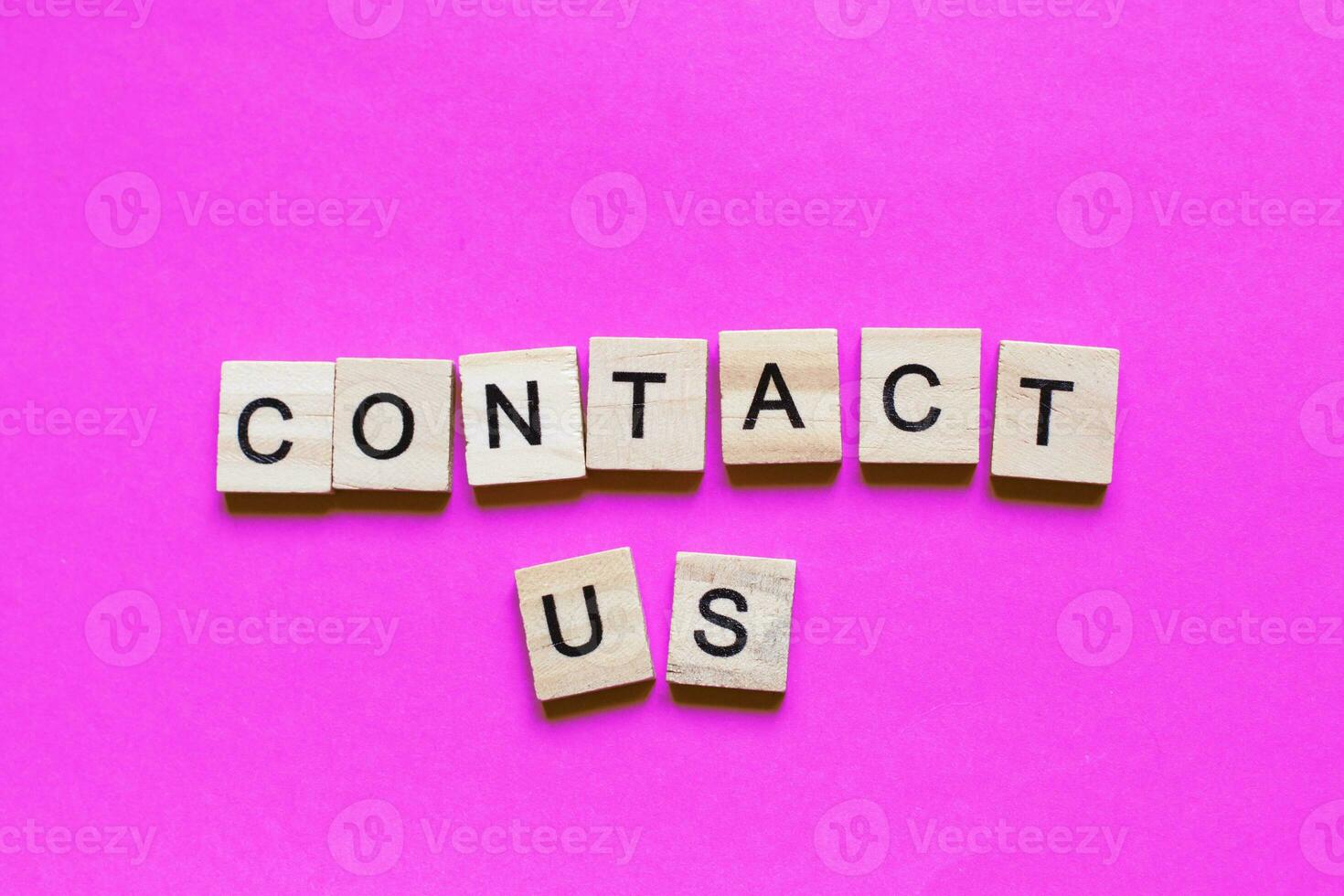 Word contact us made from wooden cubes on a pink paper background. photo