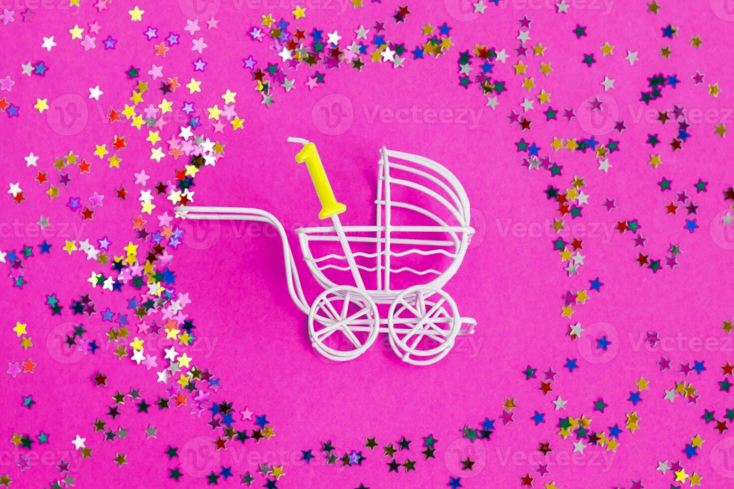 One year birthday.baby stroller with candle in form of the number one on a pink background with stars confetti sequins photo