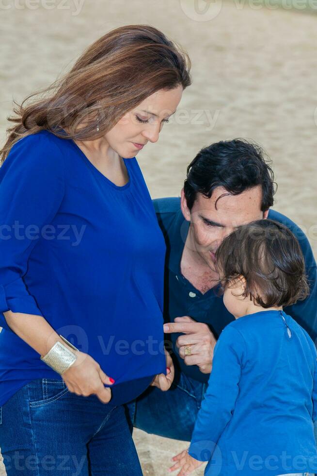 Young couple waiting for their second baby having fun with their baby girl at the beautiful white beach of Lake Tota located in the department of Boyaca at 3,015 meters above sea level in Colombia photo