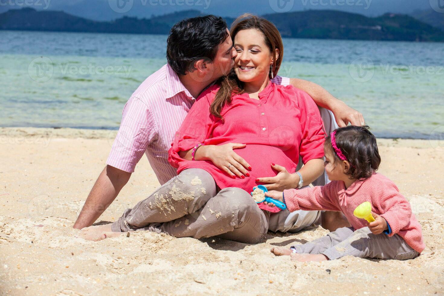Young couple waiting for their second baby having fun with their baby girl at the beautiful white beach of Lake Tota located in the department of Boyaca at 3,015 meters above sea level in Colombia photo