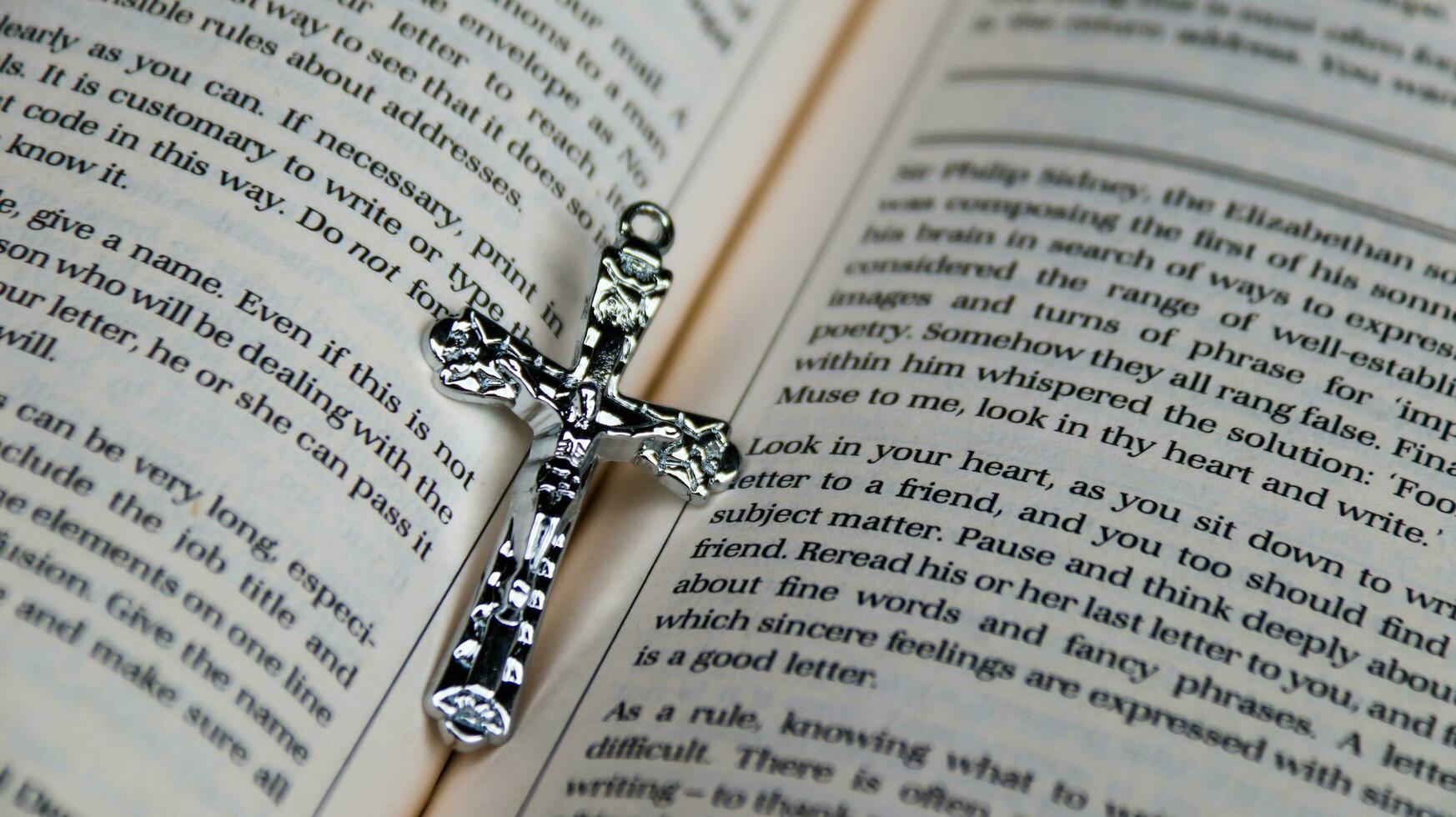 Close up shiny metal cross with black sling on old book to recall the kindness of Jesus Christ for all of Christian photo