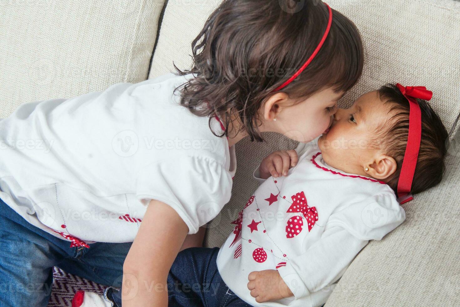 Big sister kisses her one month old baby sister at home. Love between sibblins concpet. Family concept. photo