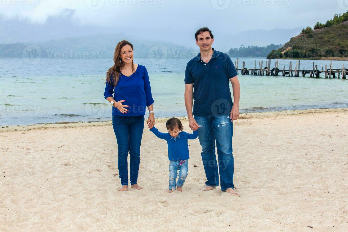 Young couple waiting for their second baby having fun with their baby girl at the beautiful white beach of Lake Tota located in the department of Boyaca at 3,015 meters above sea level in Colombia photo