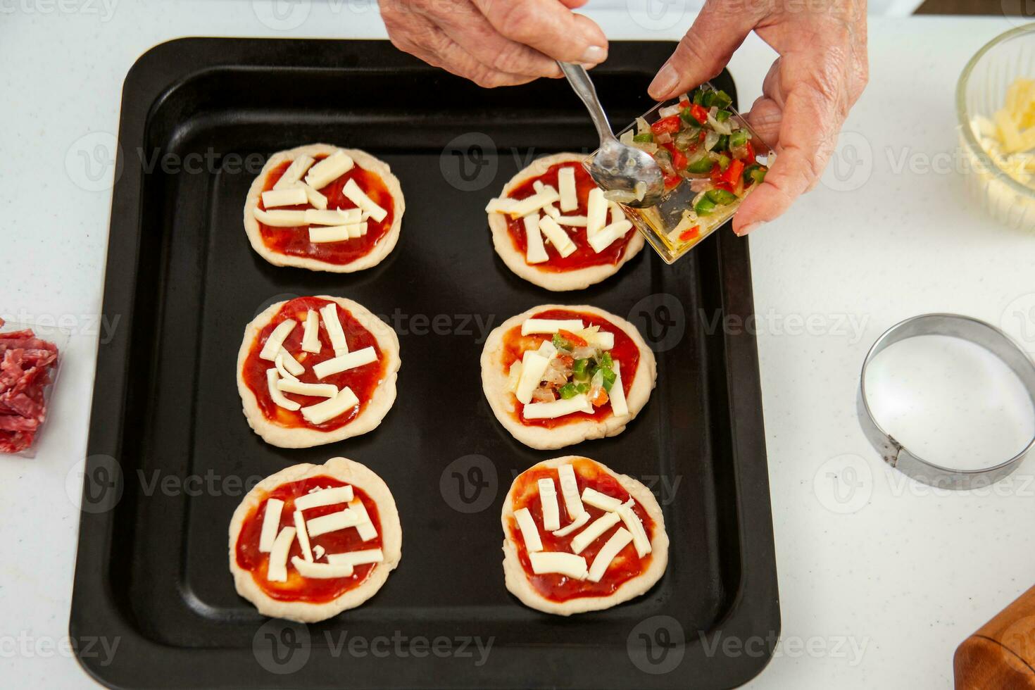 Adding toppings to the mini pizzas. Adding vegetables. Delicious homemade mini pizzas preparation. photo