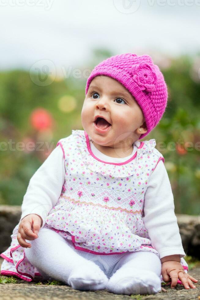 Sweet six months old baby girl sitting at the garden in a beautiful sunny day photo