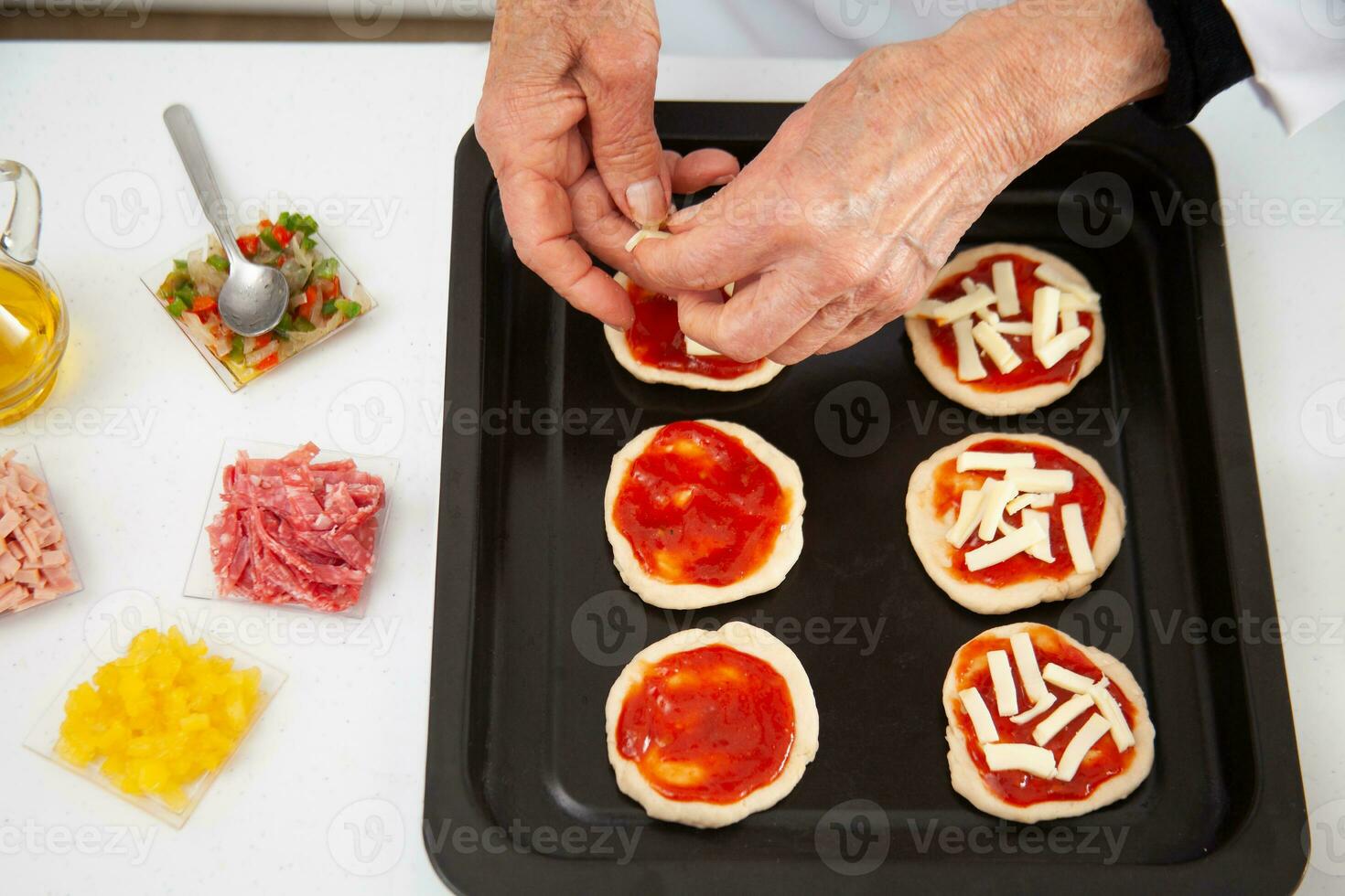 Adding toppings to the mini pizzas. Adding cheese. Delicious homemade mini pizzas preparation. photo