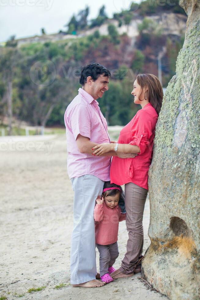 Young couple waiting for their second baby having fun with their baby girl at the beautiful white beach of Lake Tota located in the department of Boyaca at 3,015 meters above sea level in Colombia photo