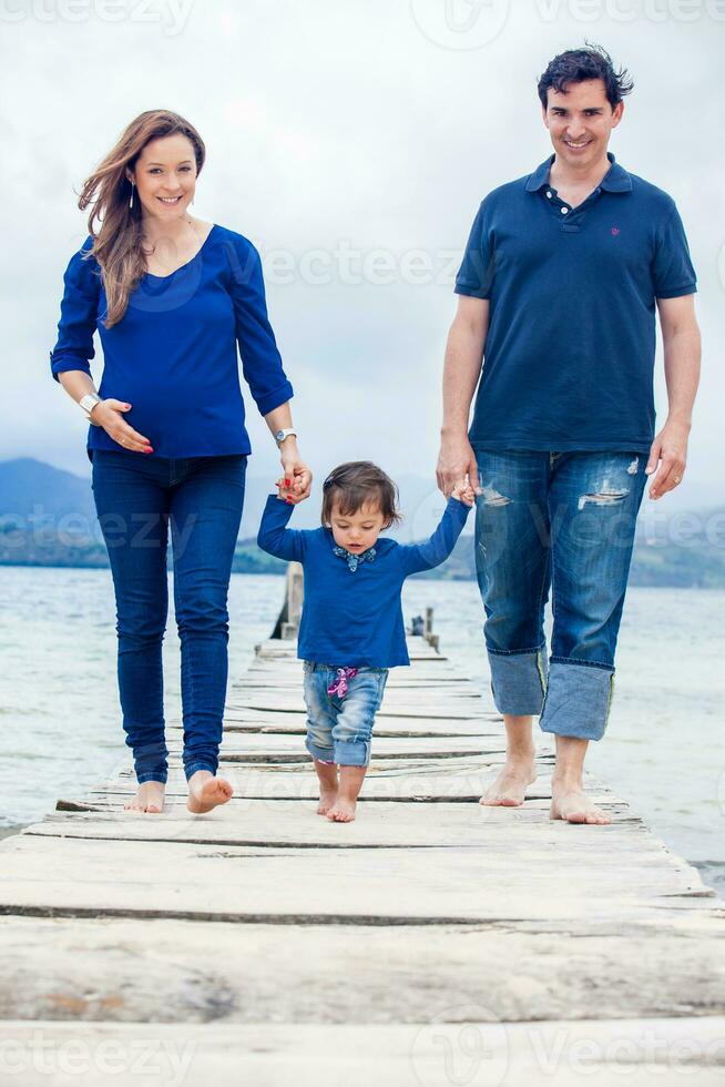Young couple waiting for their second baby having fun with their baby girl at the beautiful white beach of Lake Tota located in the department of Boyaca at 3,015 meters above sea level in Colombia photo