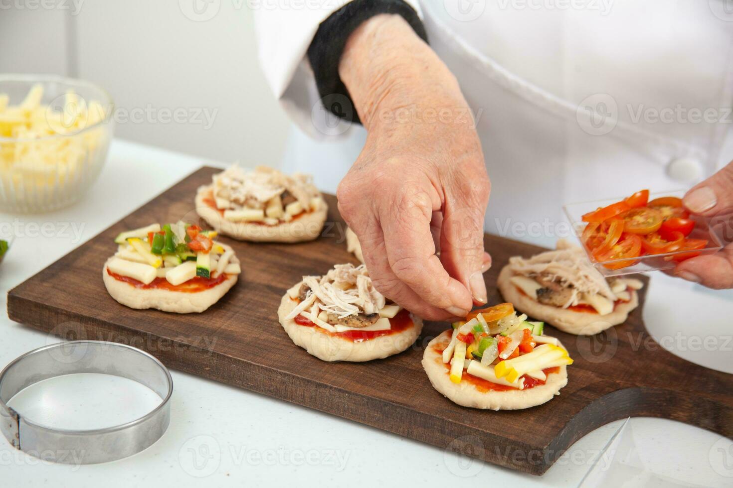 Adding toppings to the mini pizzas. Delicious homemade mini pizzas preparation. photo