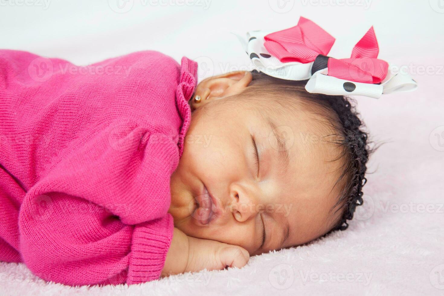 Closeup of a sweet little one month baby sleeping dressed in pink wearing a bow photo