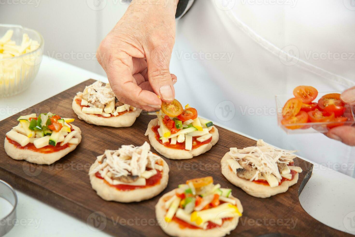 Adding toppings to the mini pizzas. Delicious homemade mini pizzas preparation. photo