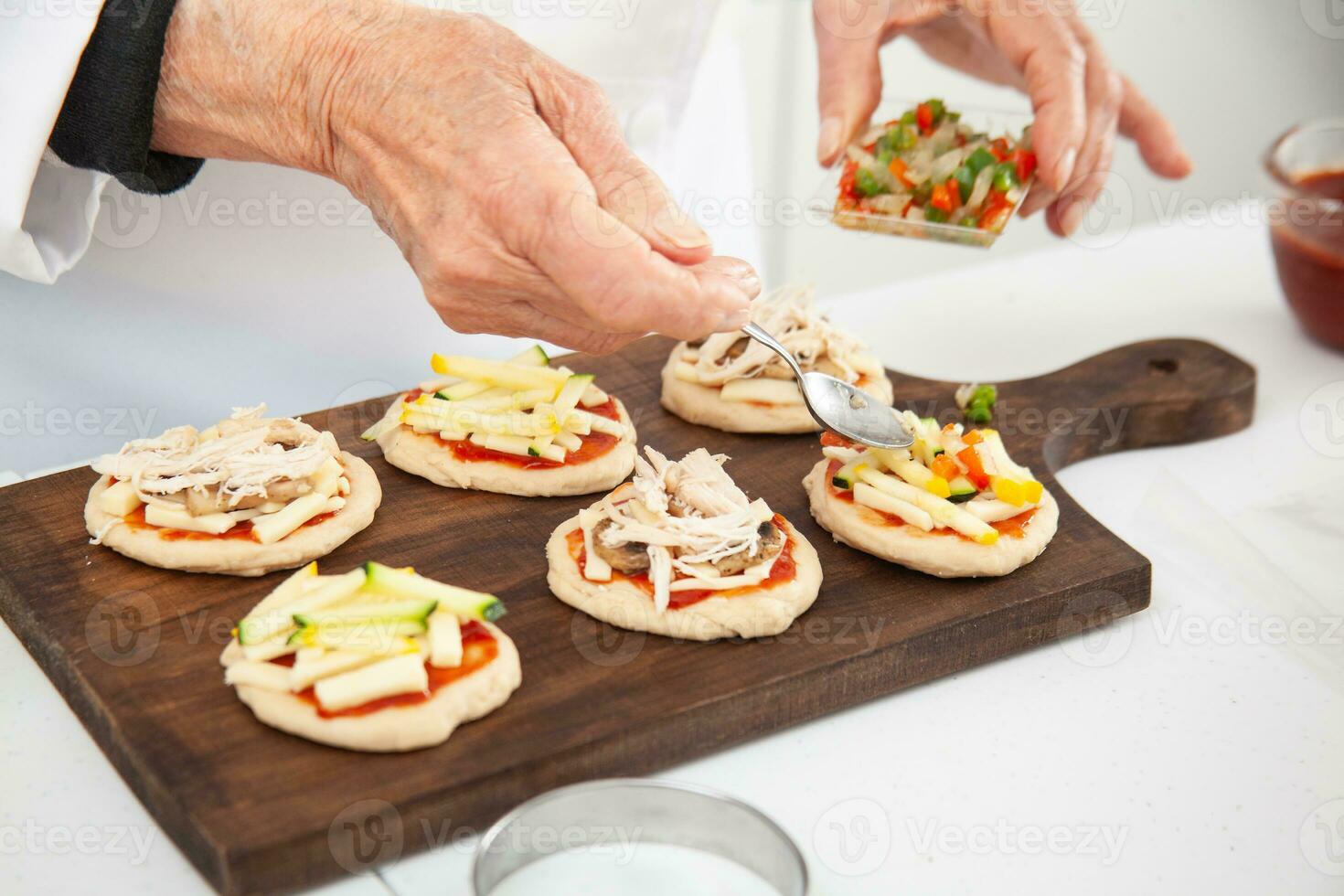 Adding toppings to the mini pizzas. Adding vegetables. Delicious homemade mini pizzas preparation. photo