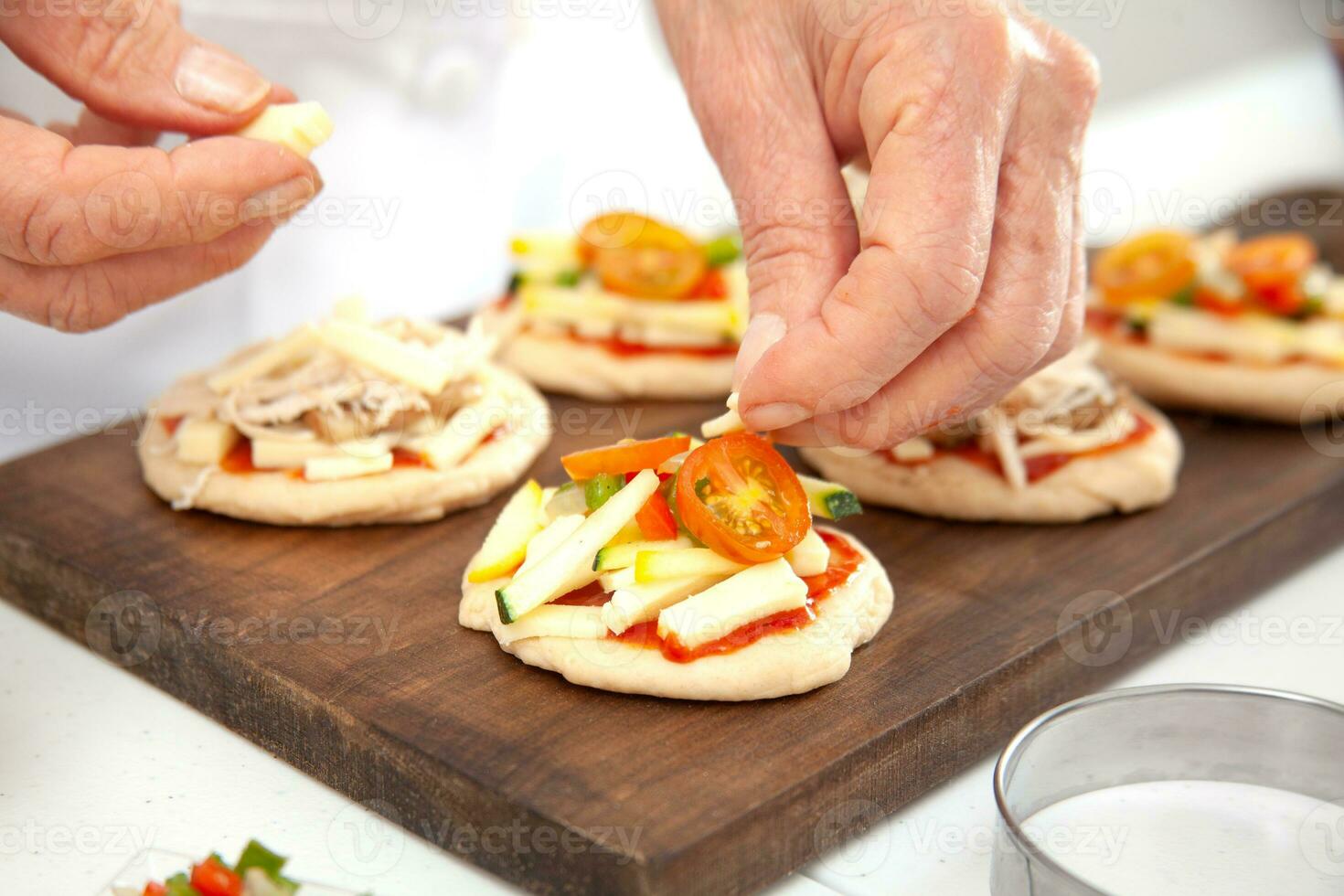 Adding toppings to the mini pizzas. Delicious homemade mini pizzas preparation. photo