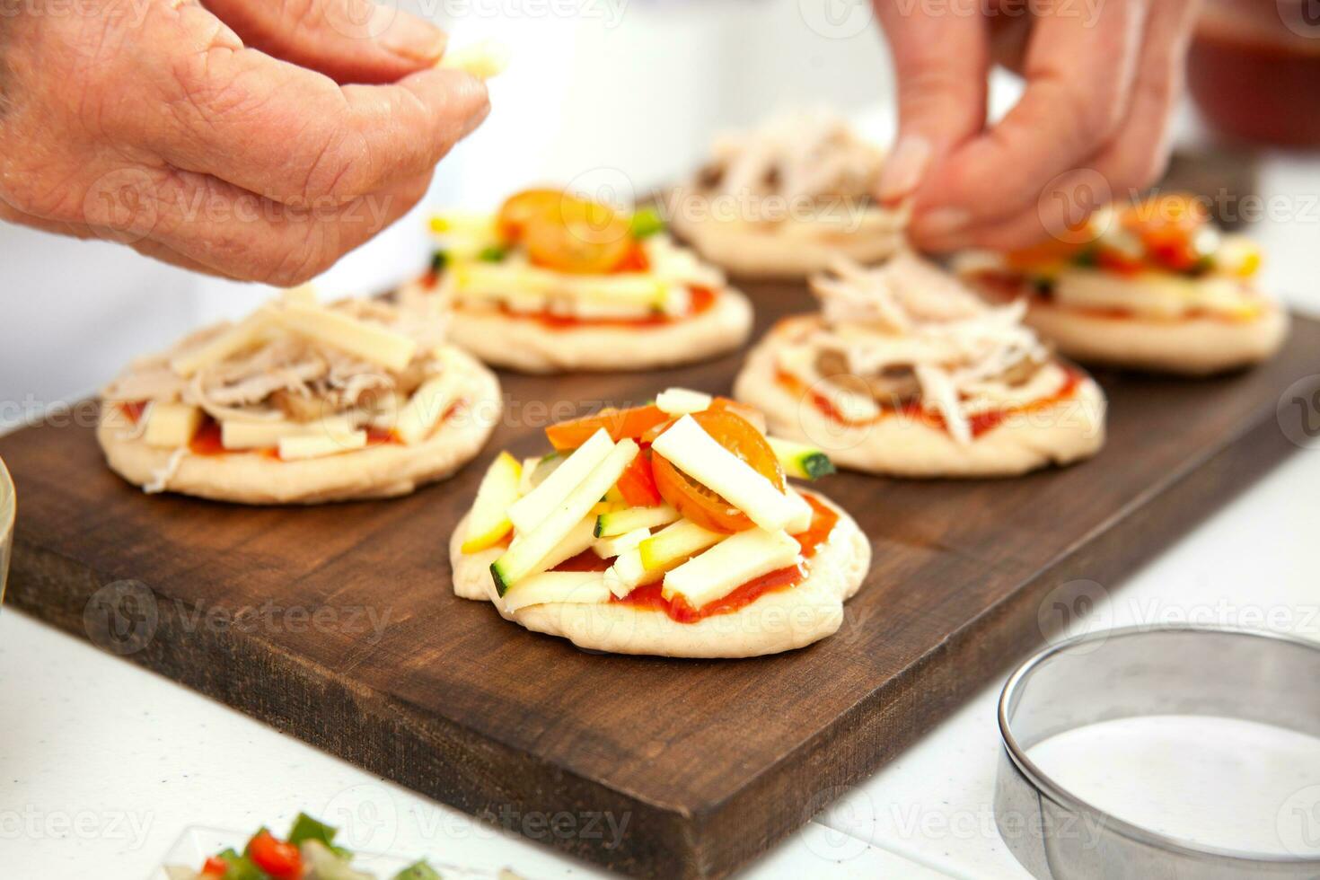 Adding toppings to the mini pizzas. Delicious homemade mini pizzas preparation. photo