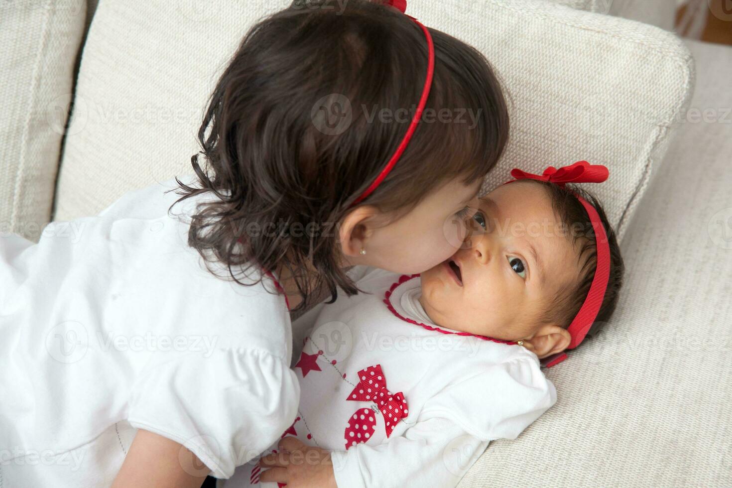 One month old baby girl being kissed by her big sister at home. Love between siblings concept. Family concept. photo