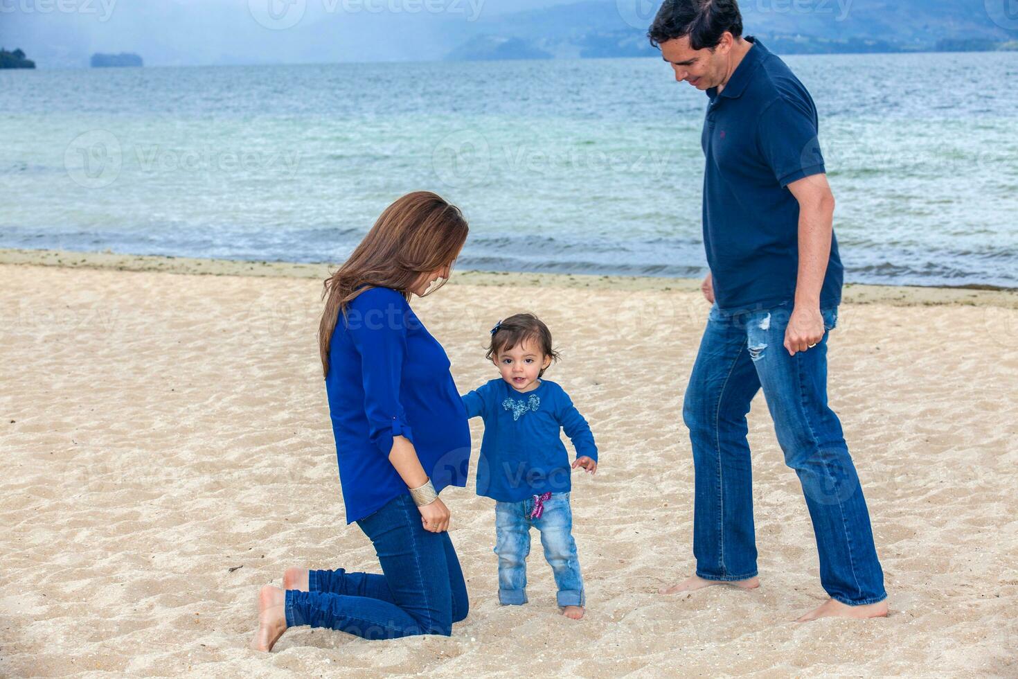 Young couple waiting for their second baby having fun with their baby girl at the beautiful white beach of Lake Tota located in the department of Boyaca at 3,015 meters above sea level in Colombia photo