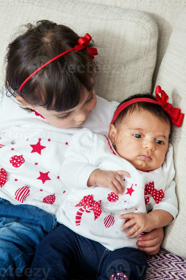 One month old baby girl at home with her big sister. Love between siblings concept. Family concept. photo