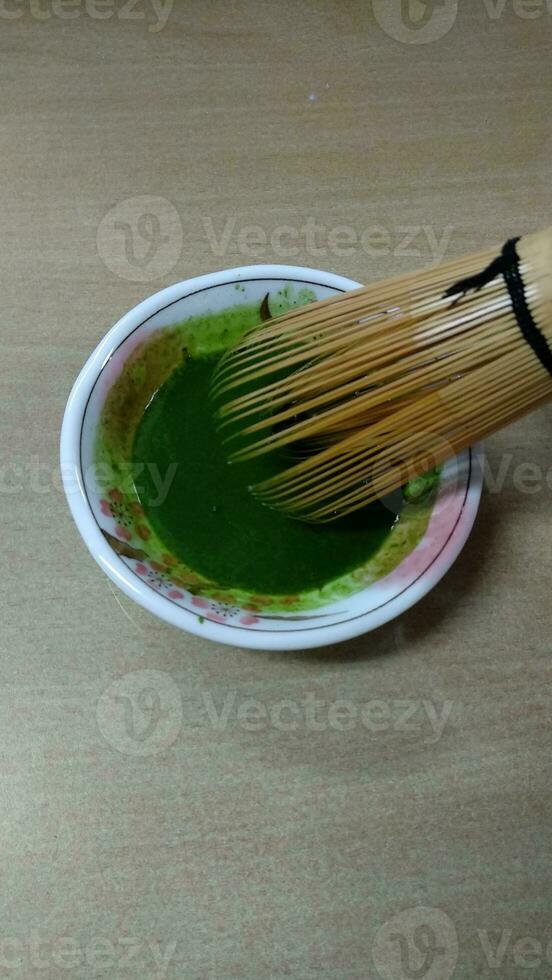 Matcha green tea in a bowl with bamboo whisk, close up photo