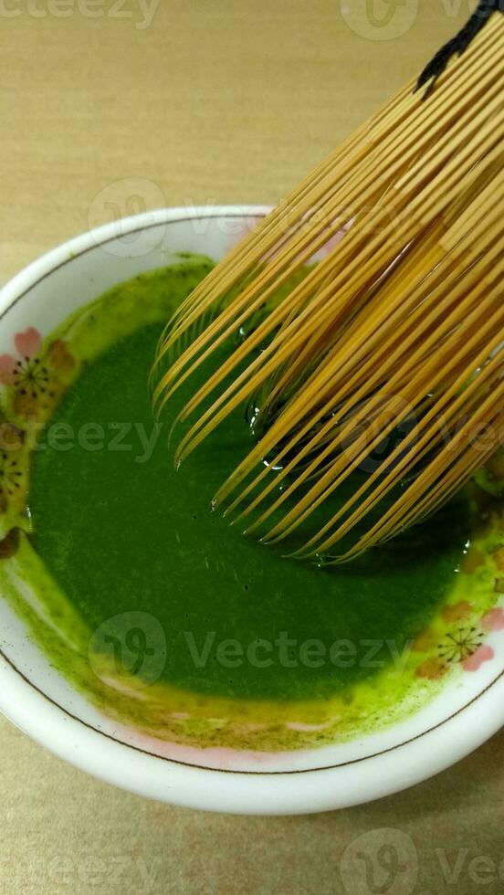 Matcha green tea in a bowl with bamboo whisk, close up photo