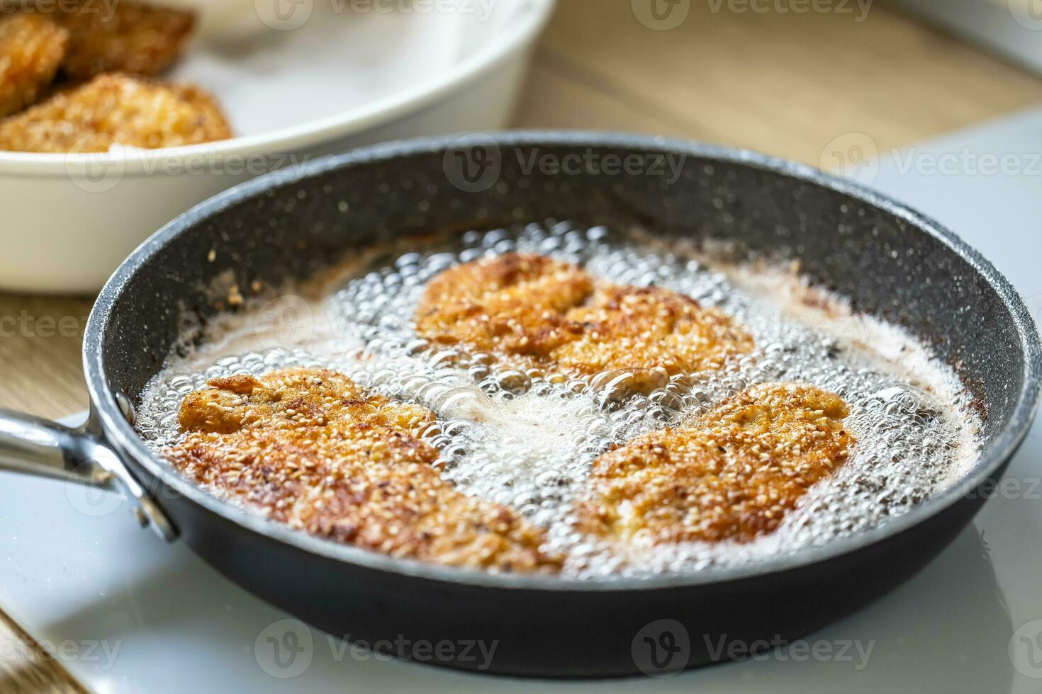 Sizzling hot oil with schnitzel frying in it in a dark pan photo