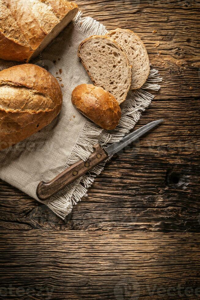parte superior ver de Tres rebanadas de crujiente horneado un pan en un Clásico paño y de madera antecedentes con un cuchillo en el lado foto