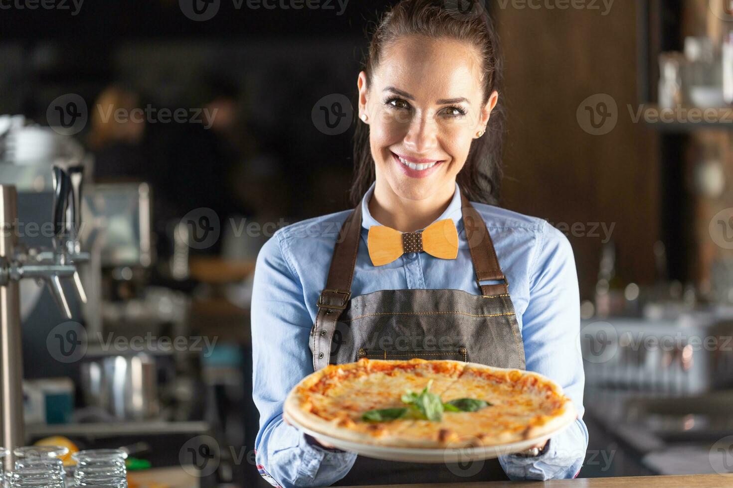 Waitress smiles while serving large authentic Italian pizza in a restaurant photo