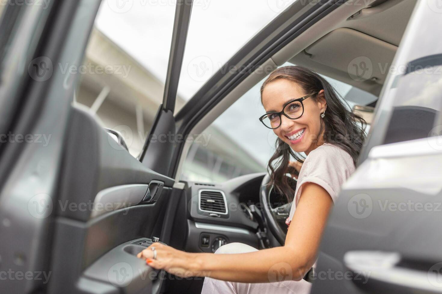 Smiling woman driver in glasses opens the car door looking backwards