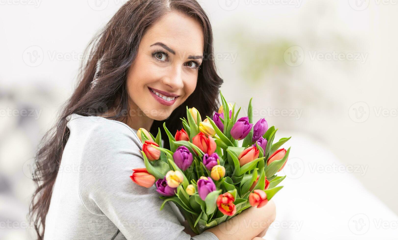 Happy dark haired woman holding a lovely bouquet full of tulips during national womens day photo