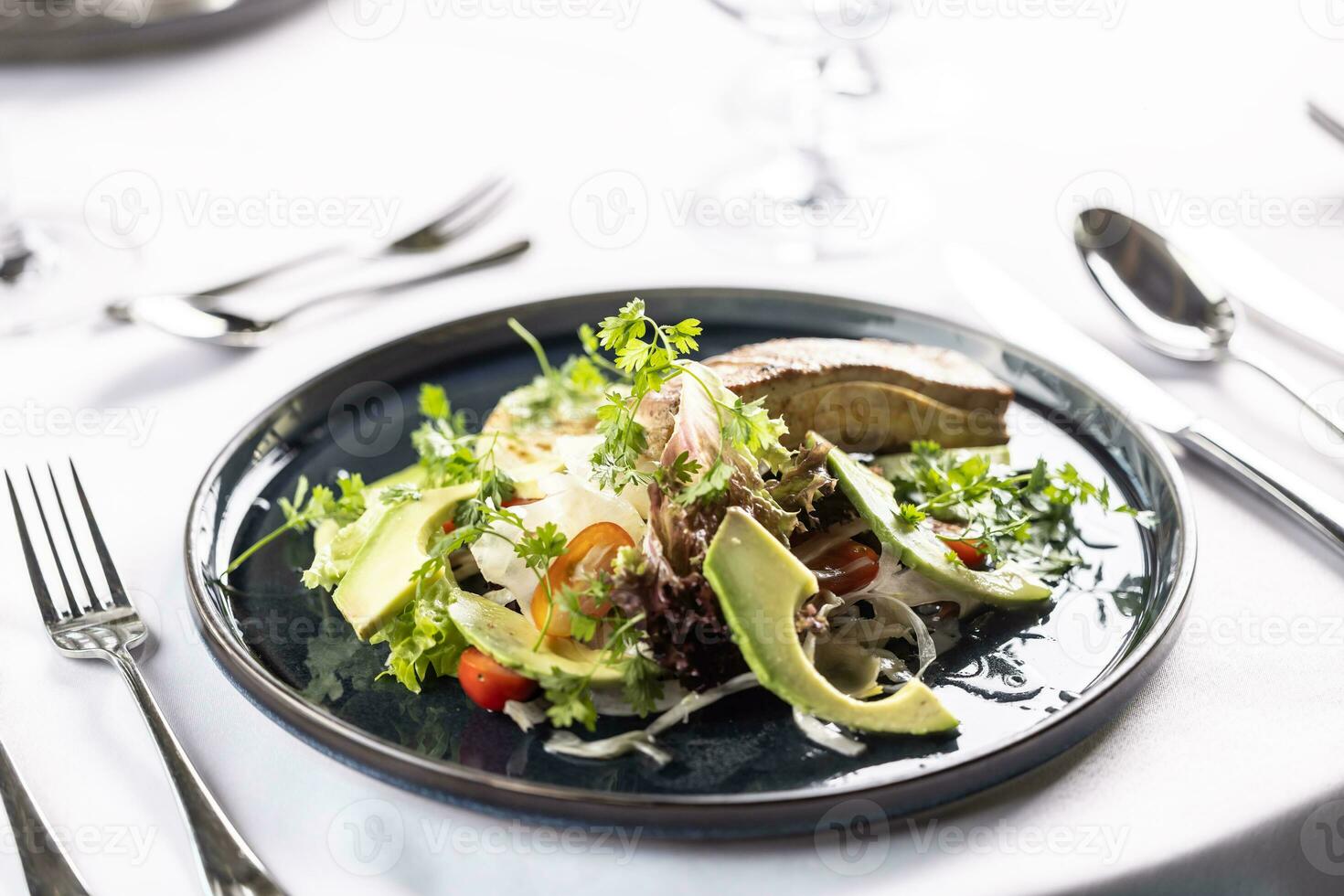 Vegetarian salad with tofu, leaves, tomatoes, and avocado on a dark plate photo