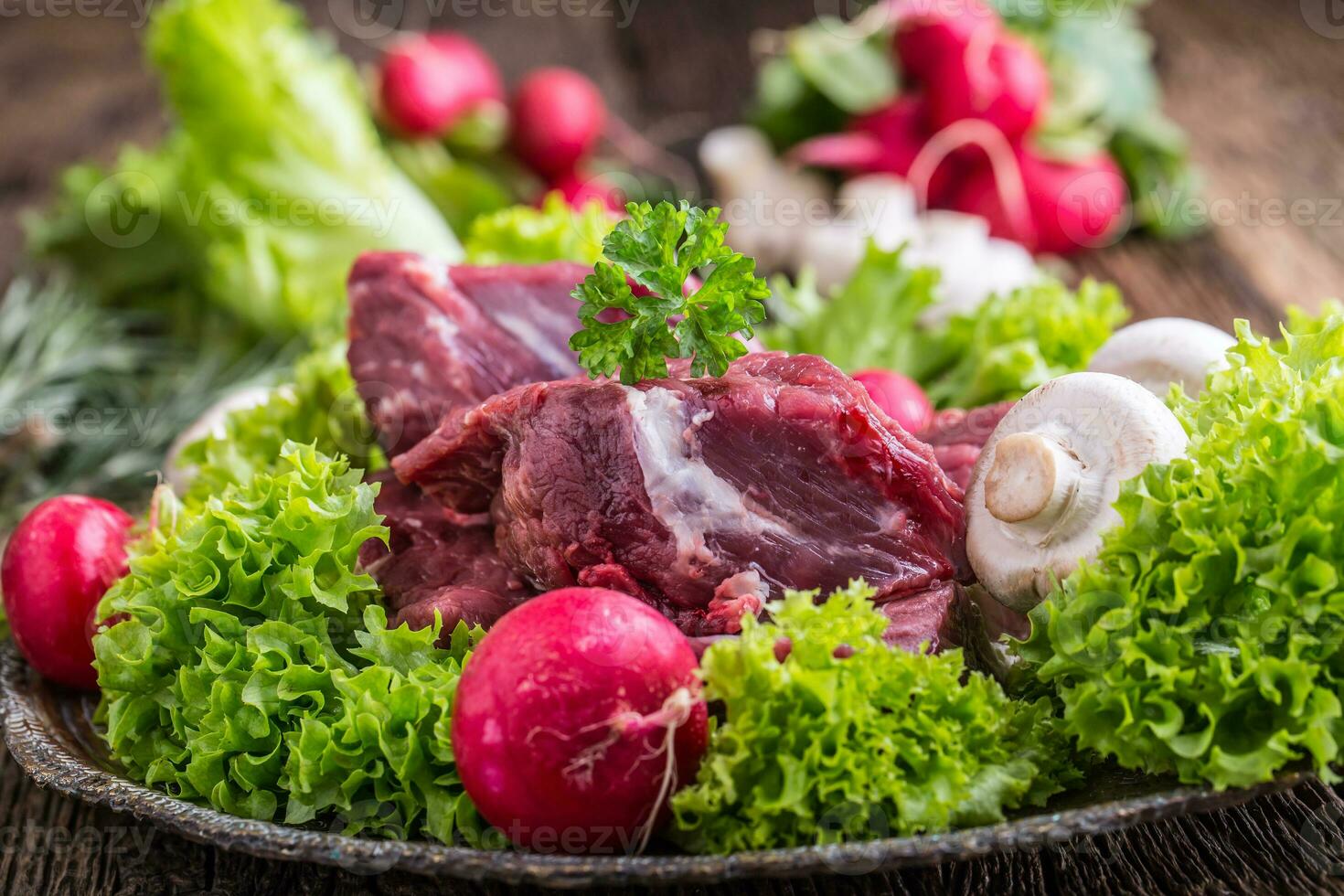 Raw beef meat with fresh vegetable. Sliced beef steak in lettuce salads radishes and mushrooms. photo