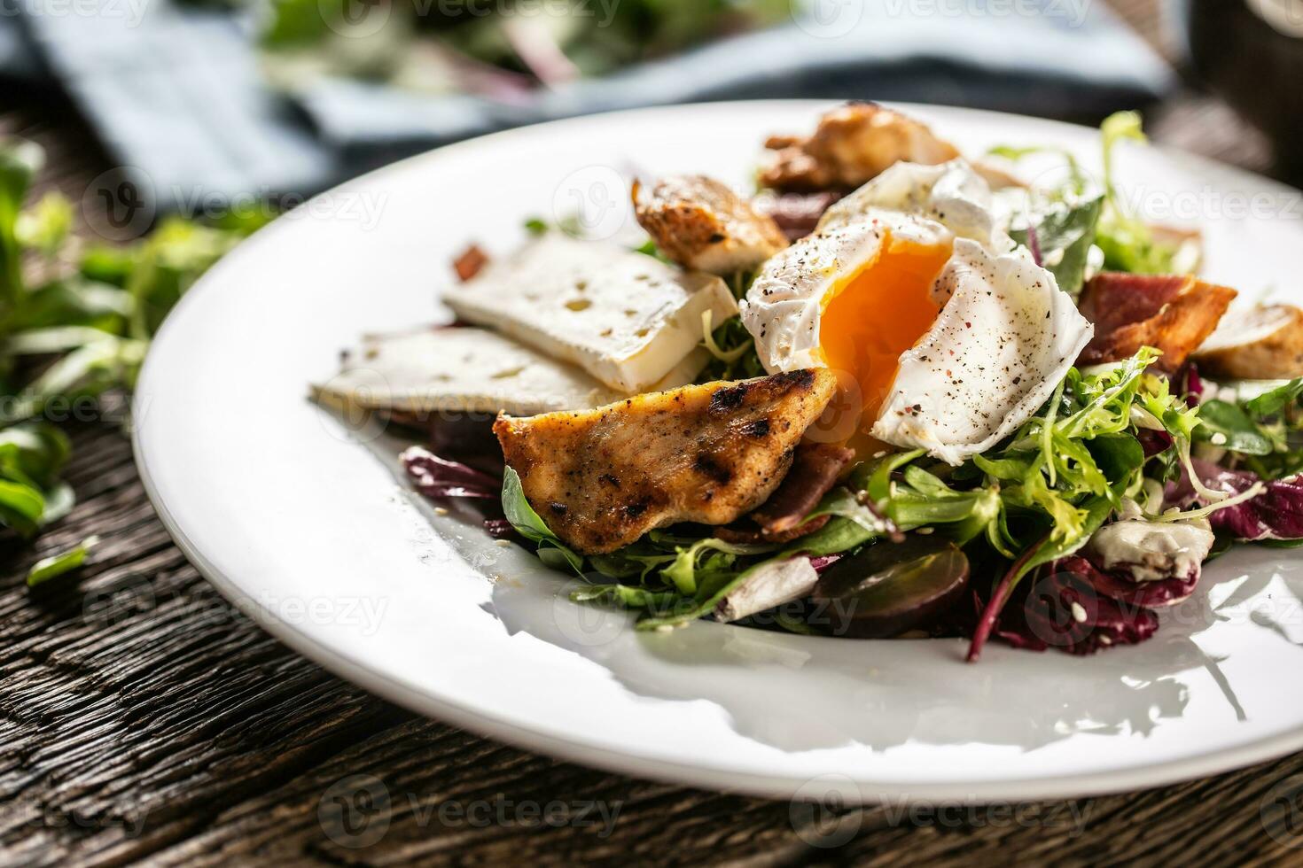 Yummy fresh summer like lettuce salad made of various types of leafs served on the plate with pieces of delicious sheep cheese, grilled crunchy chicken breasts and seasoned runny egg photo