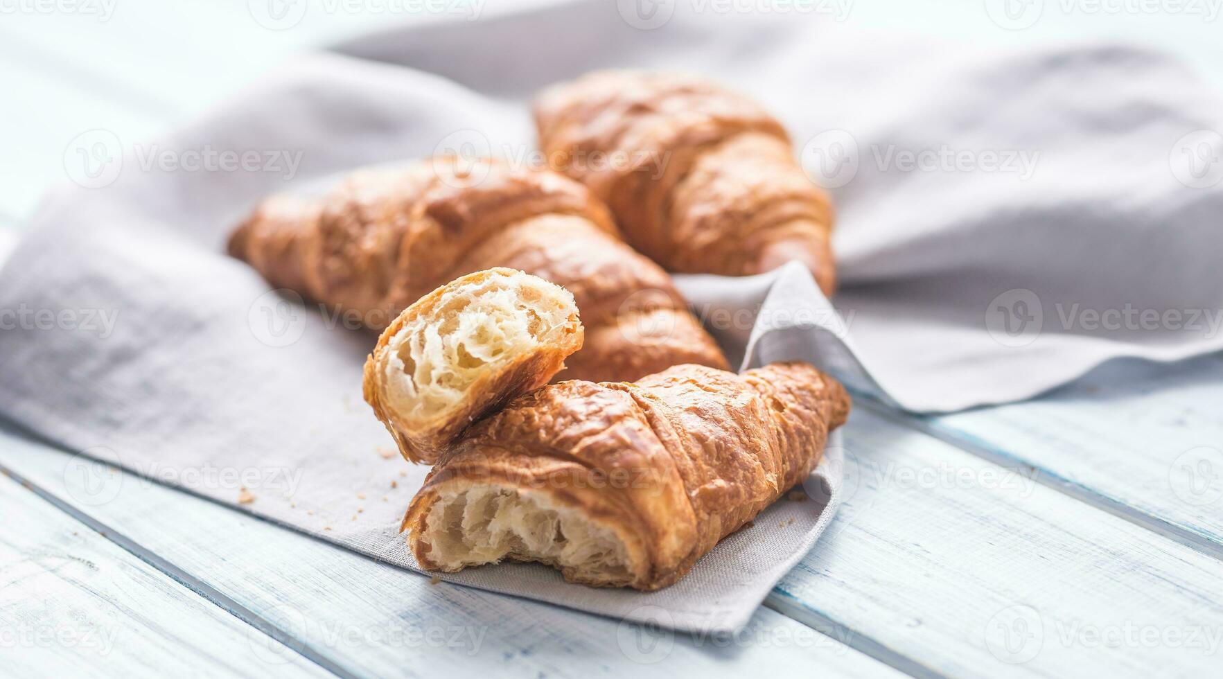 Fresh buttery croissants on kitchen napkin and wooden table photo