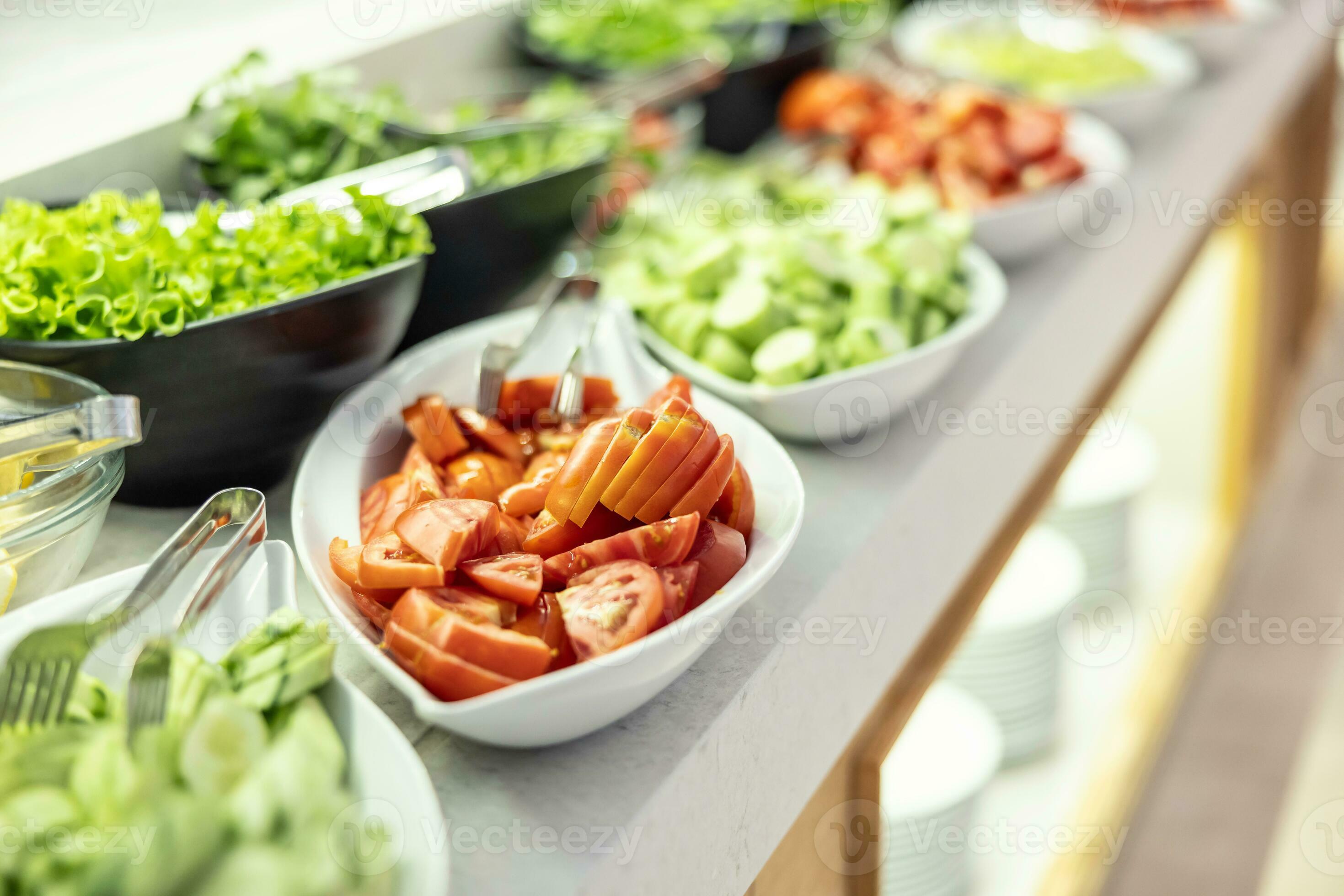 Fresh vegetables, cucumbers, tomatoes and lettuce in bowls on buffet