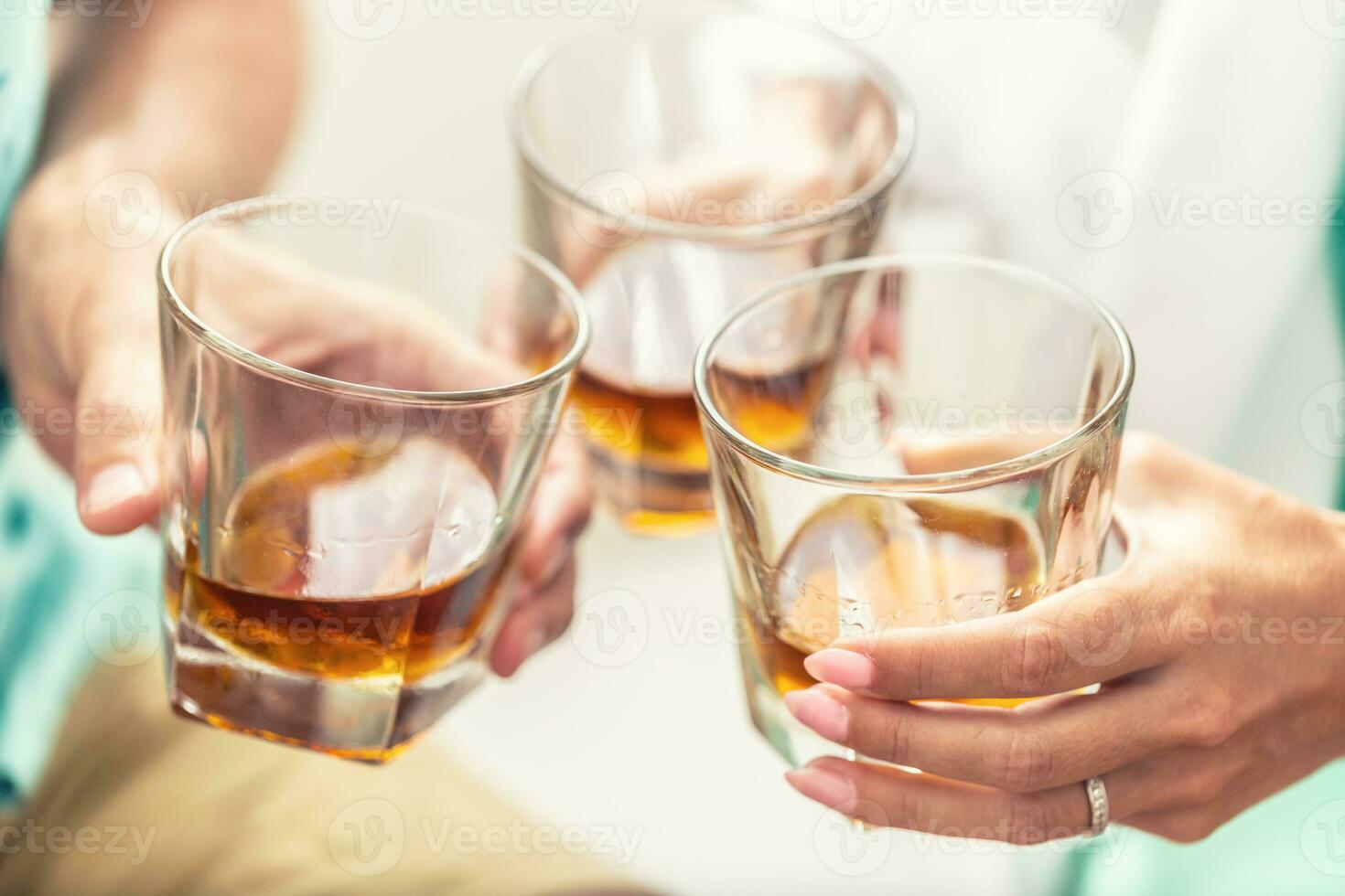 Group of friends toasting with glasses of whiskey brandy or rum indoors - closeup photo