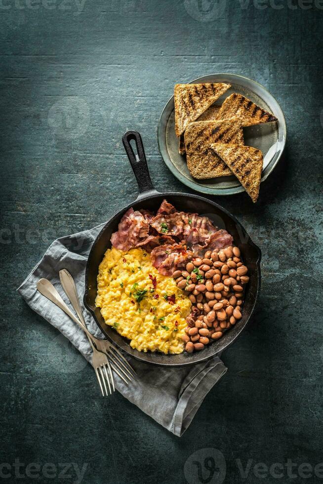 English breakfast scrambled eggs grilled bacon beans and toast bread - Top of view photo