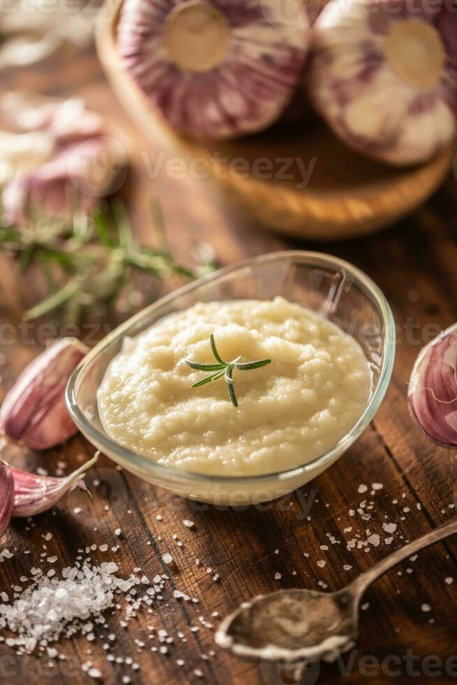 Garlic paste in a glass bowl with peeled garlic, salt and garlic heads photo