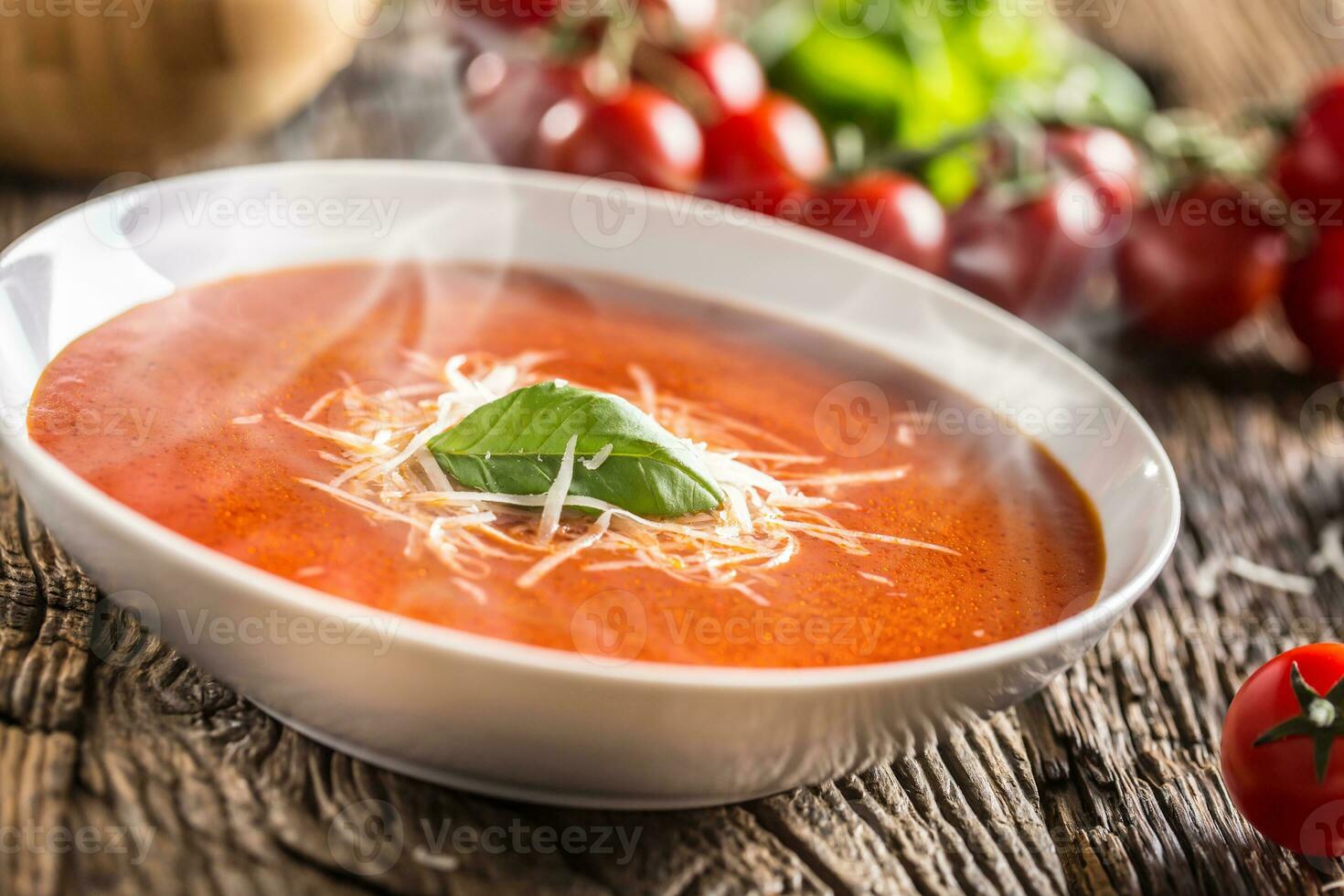 Hot tomato soup parmesan cheese and basil leave on old oal table photo