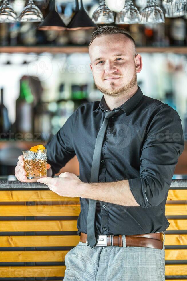 barman en pie antes de el bar y en el mano participación cóctel bebida foto