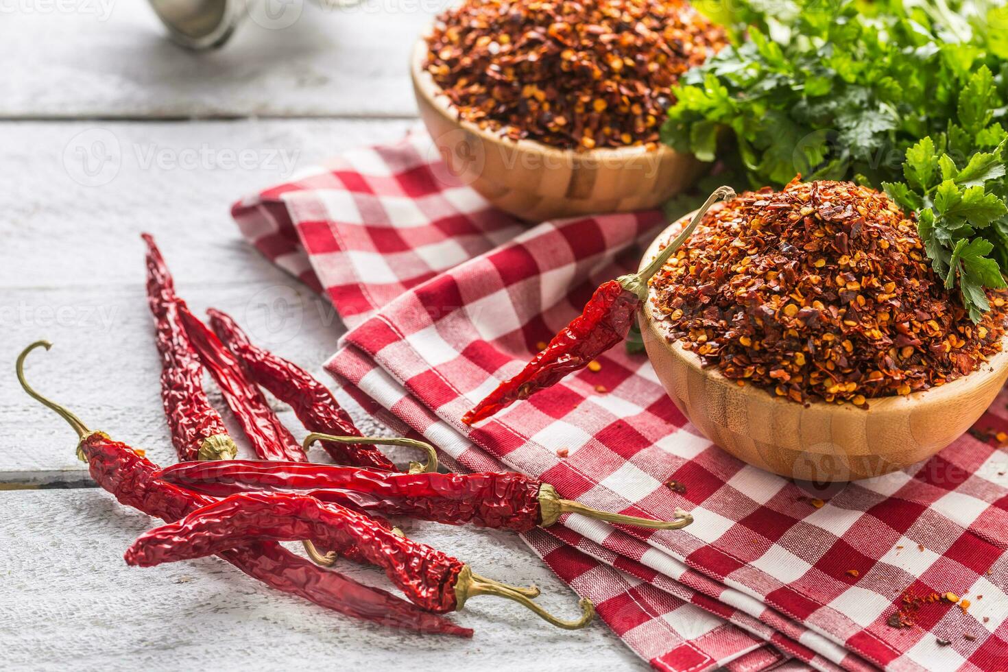 Dried and crushed chili peppers in wooden bowles with parsley herbs photo