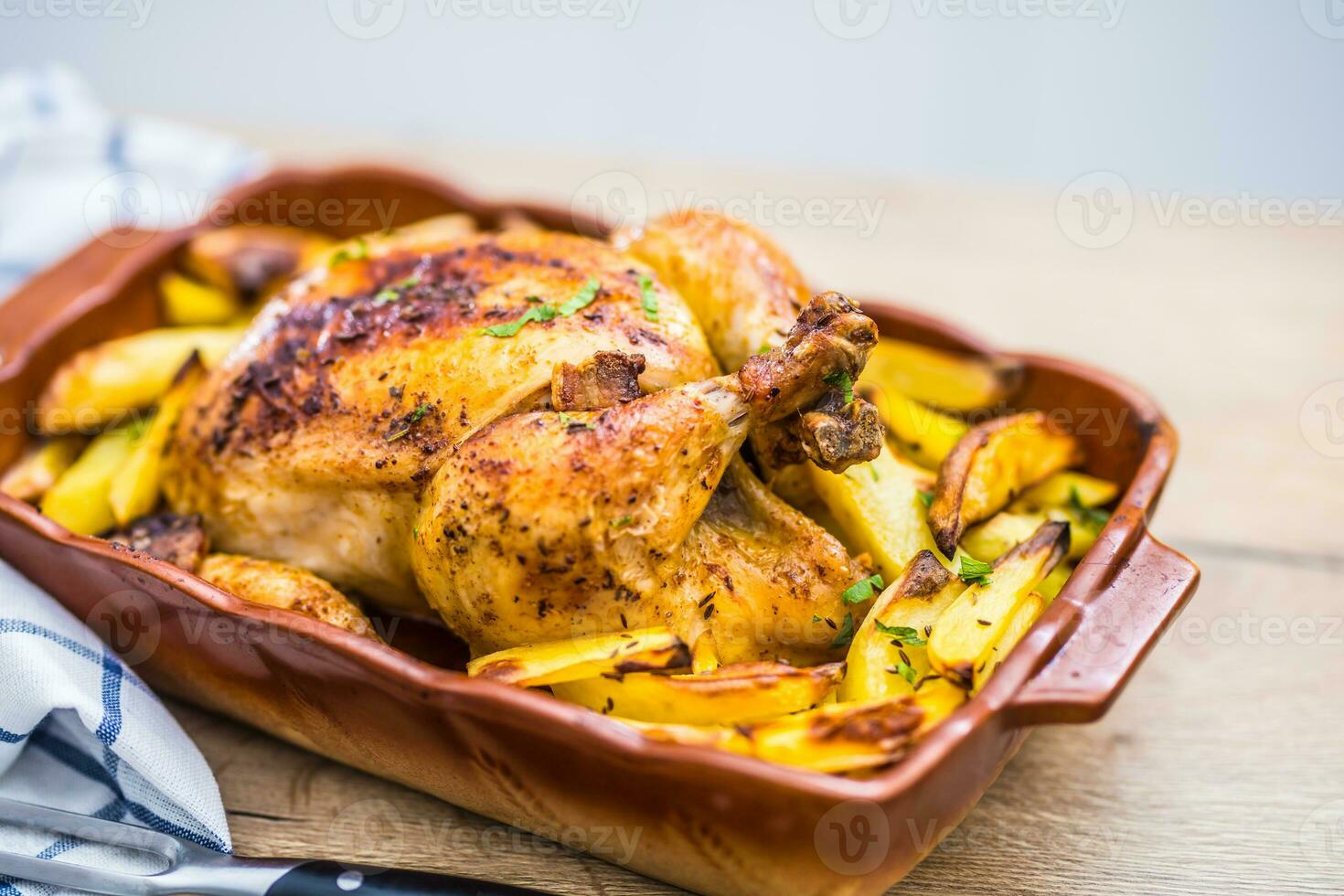 Roasted whole chicken with potatoes in baking dish. Tasty food at home on the kitchen counter photo